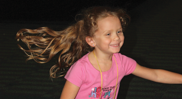 A close up of a young blind girl smiling widely with her hair flowing out behind her.