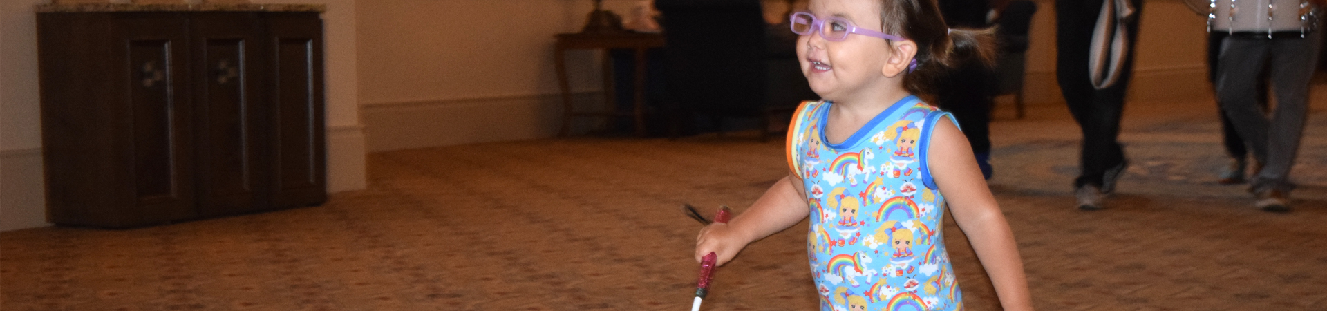 A blind toddler skips with her cane leading the way.