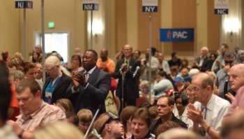 A large crowd of members stands and claps during the NFB national convention opening session.