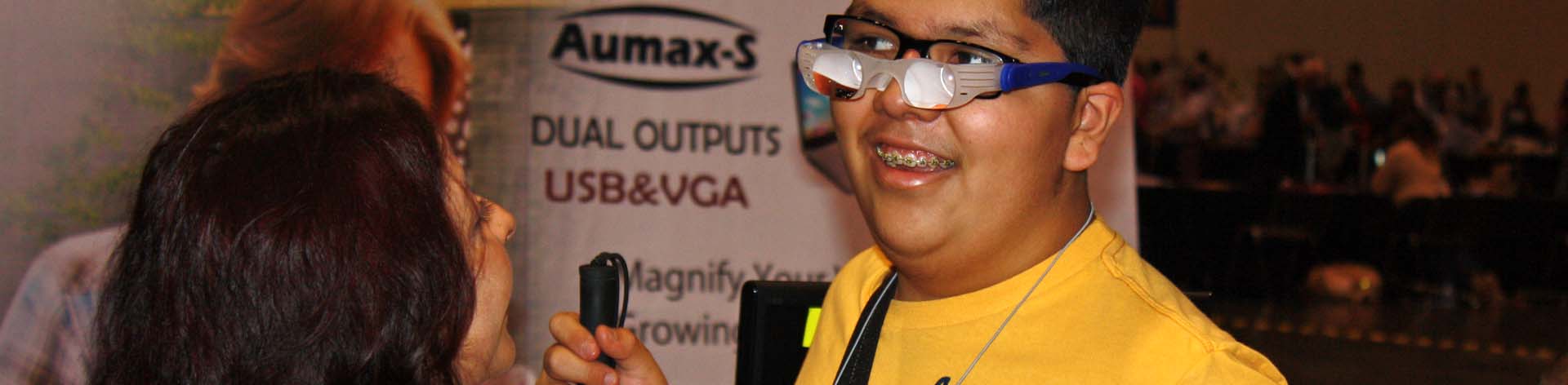 An NFB of Nevada member tests out a pair of magnifying glasses in the exhibit hall at a national convention