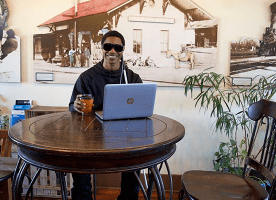 Blind man sits at table with coffee and a laptop