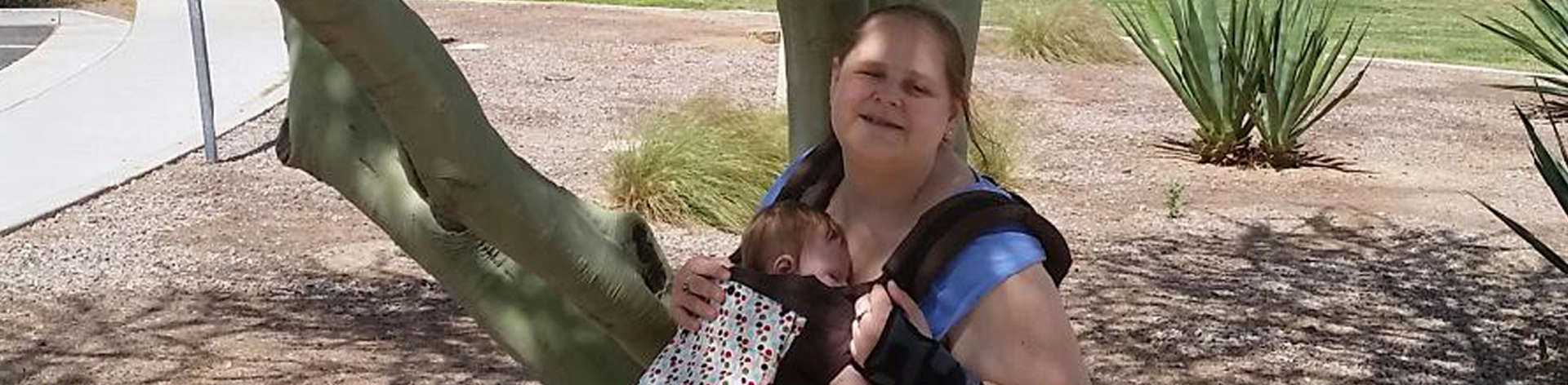 A blind mom smiles with her child in a carrier.